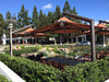 Outdoor seating area with tables and chairs under large USA Shade Solana Cantilevers in a park-like setting.