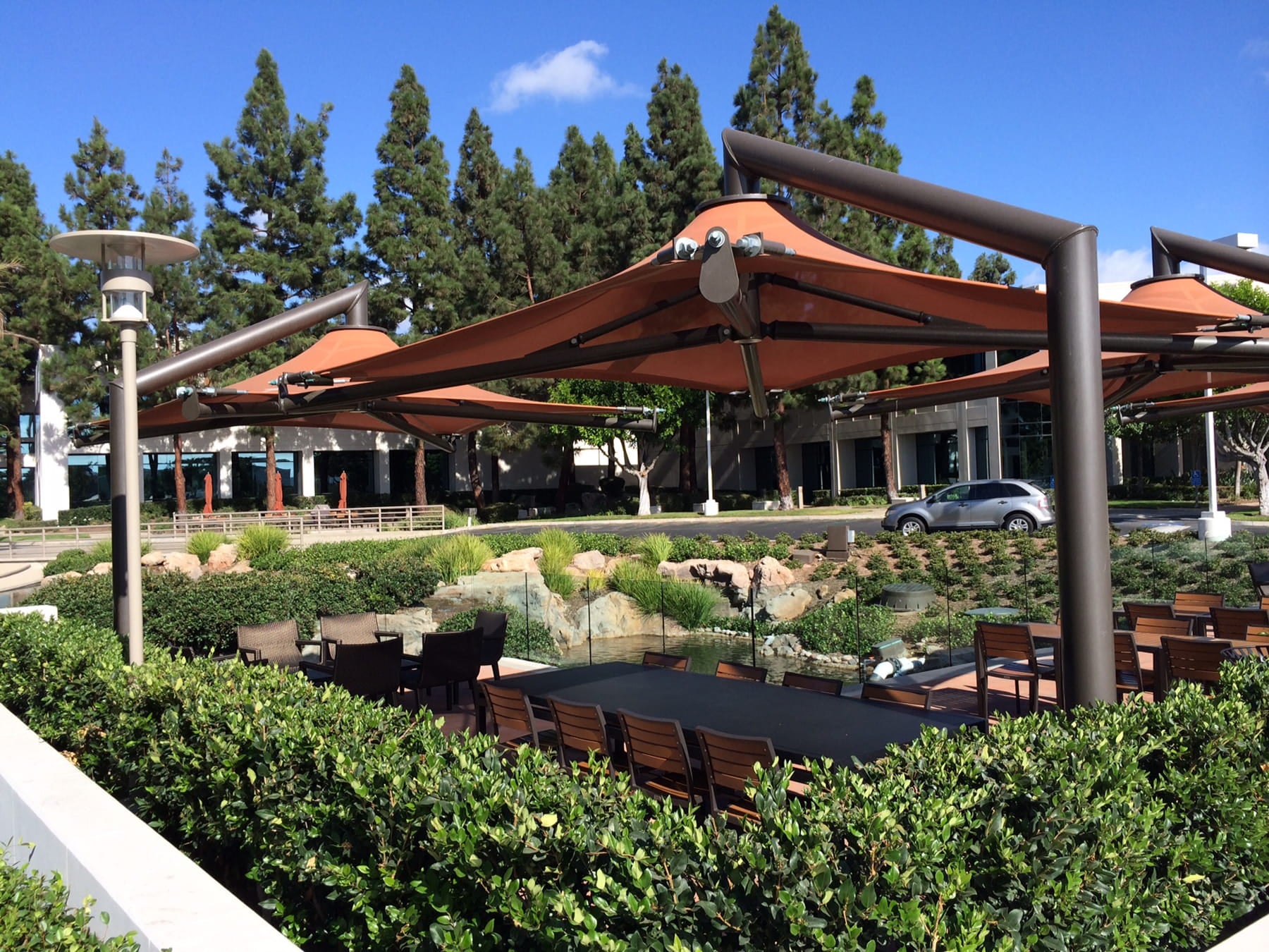 Outdoor seating area with tables and chairs under large USA Shade Solana Cantilevers in a park-like setting.