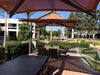Outdoor seating area with tables and USA Shade Solana Cantilevers under a clear blue sky.