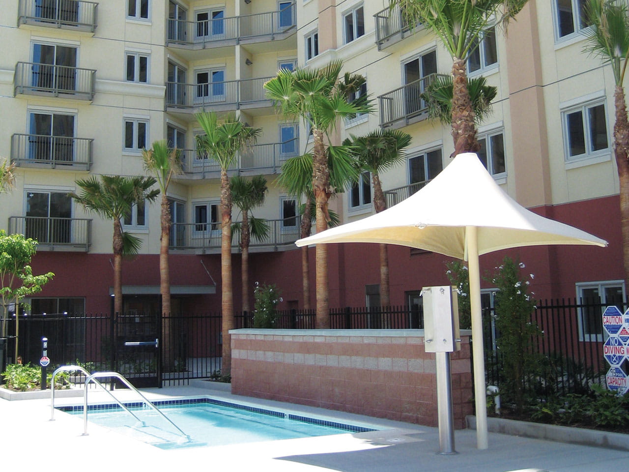 Pool area with a white USA Shade Lifeguard Umbrella and palm trees in front of a building