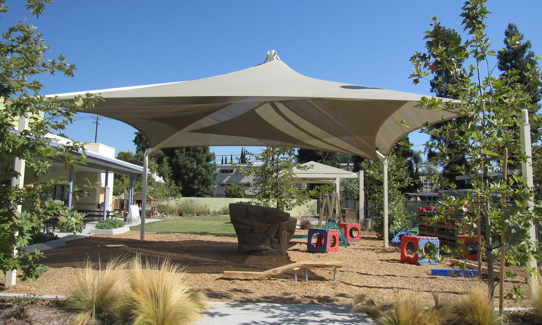 Large outdoor USA Shade Mariner Pyramid Shade structure with trees and garden elements in the background