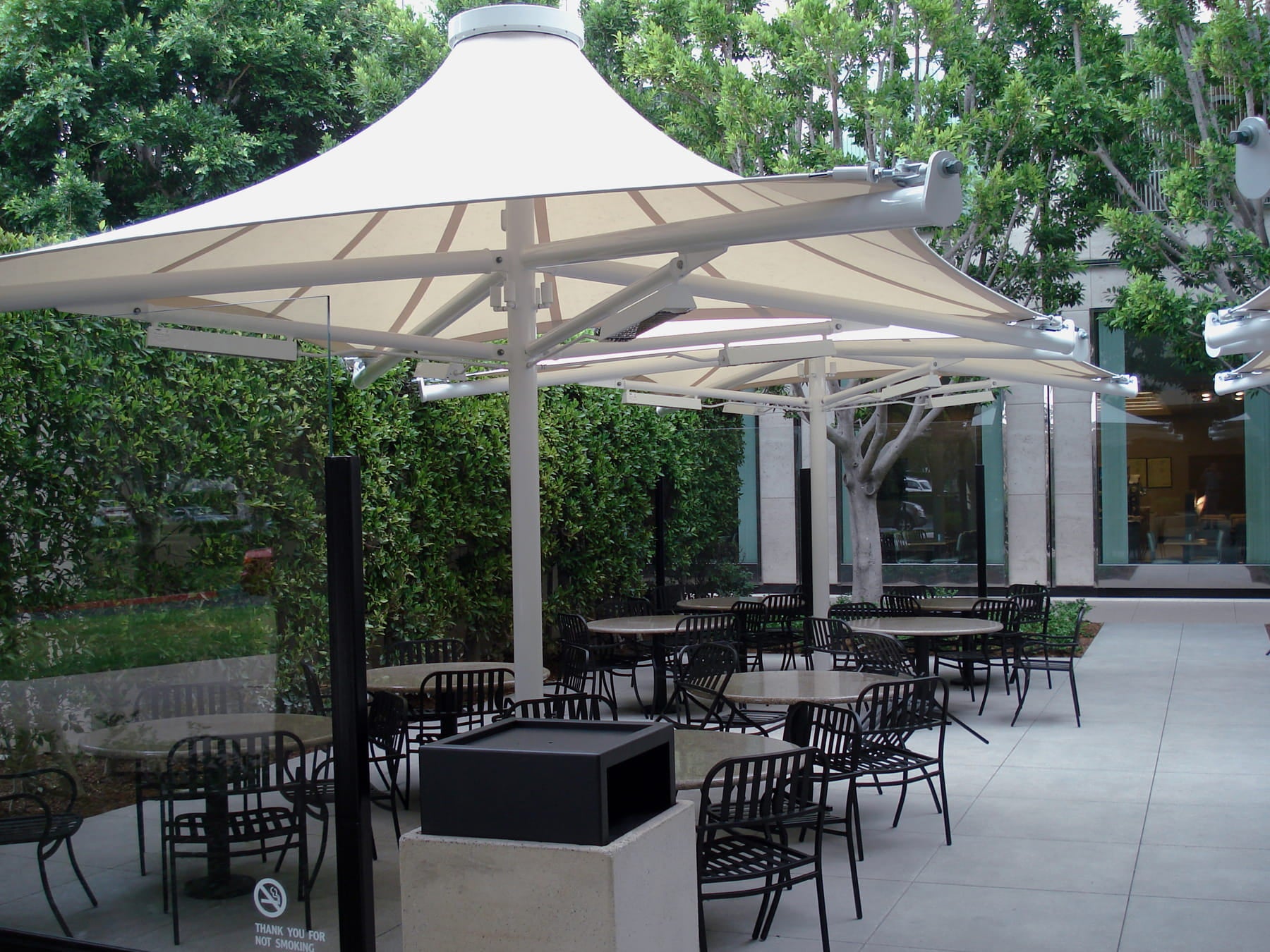 Outdoor seating area with large USA Shade 4-point Twilite Umbrellas and tables under a canopy