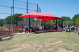Red USA Shade Wrap-around Hip providing shade at a sports field with people sitting underneath.