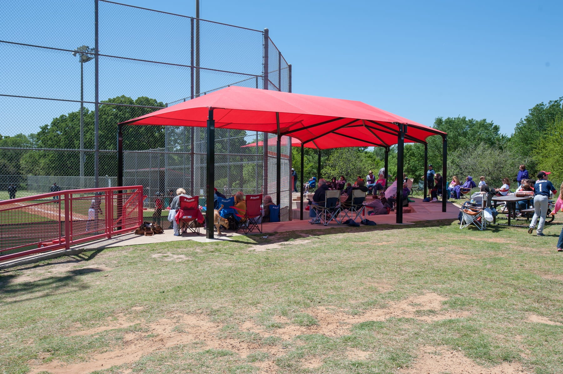 Red USA Shade Wrap-around Hip providing shade at a sports field with people sitting underneath.
