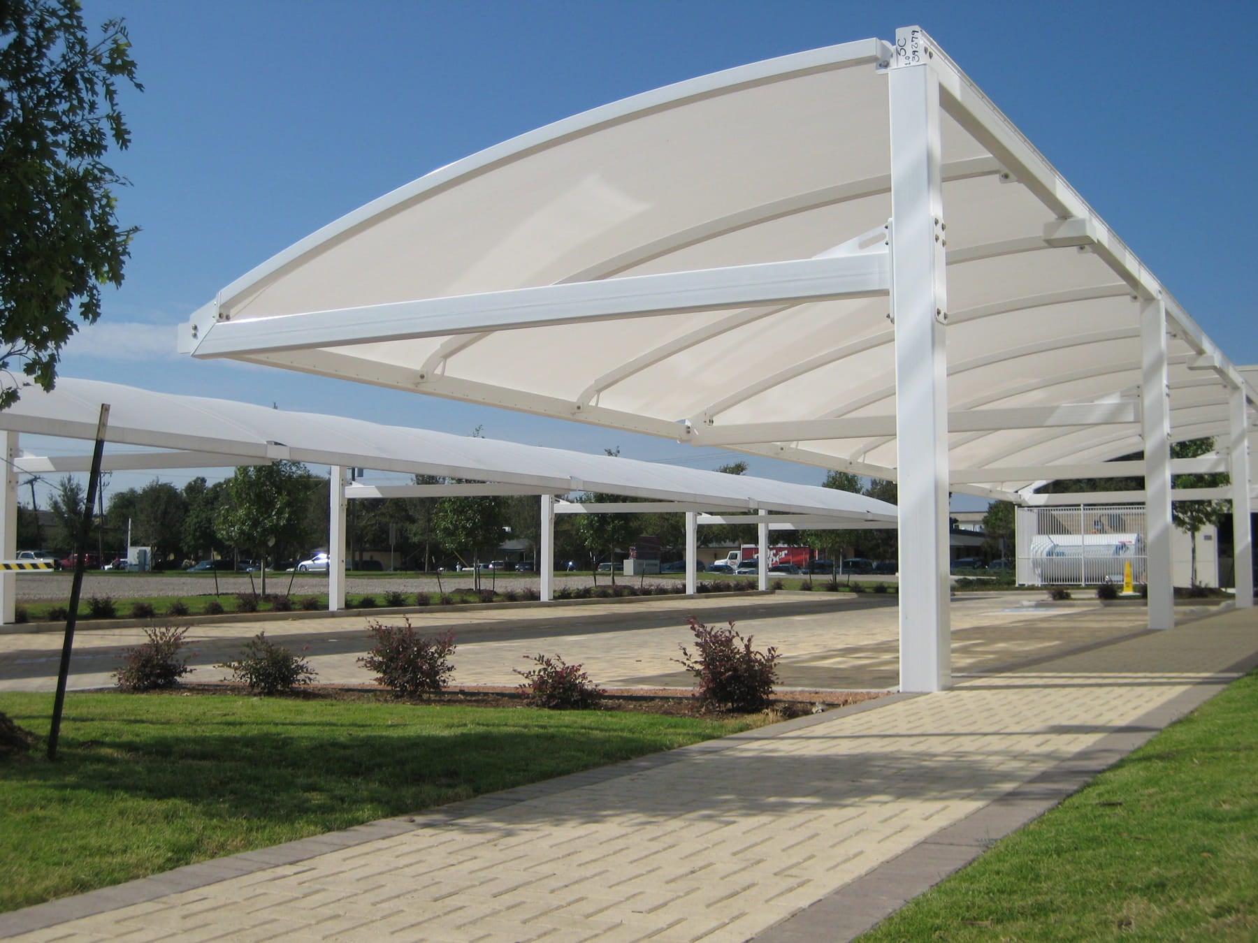 Large outdoor USA Shade Full Arch Cantilever structure with a white roof and beige walls, set against a clear blue sky.