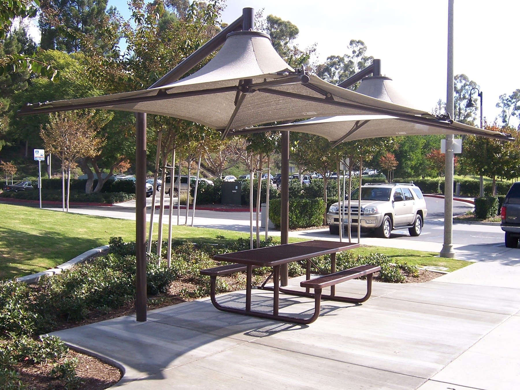 Picnic table under a large USA Shade Solana Cantilever with cars and trees in the background