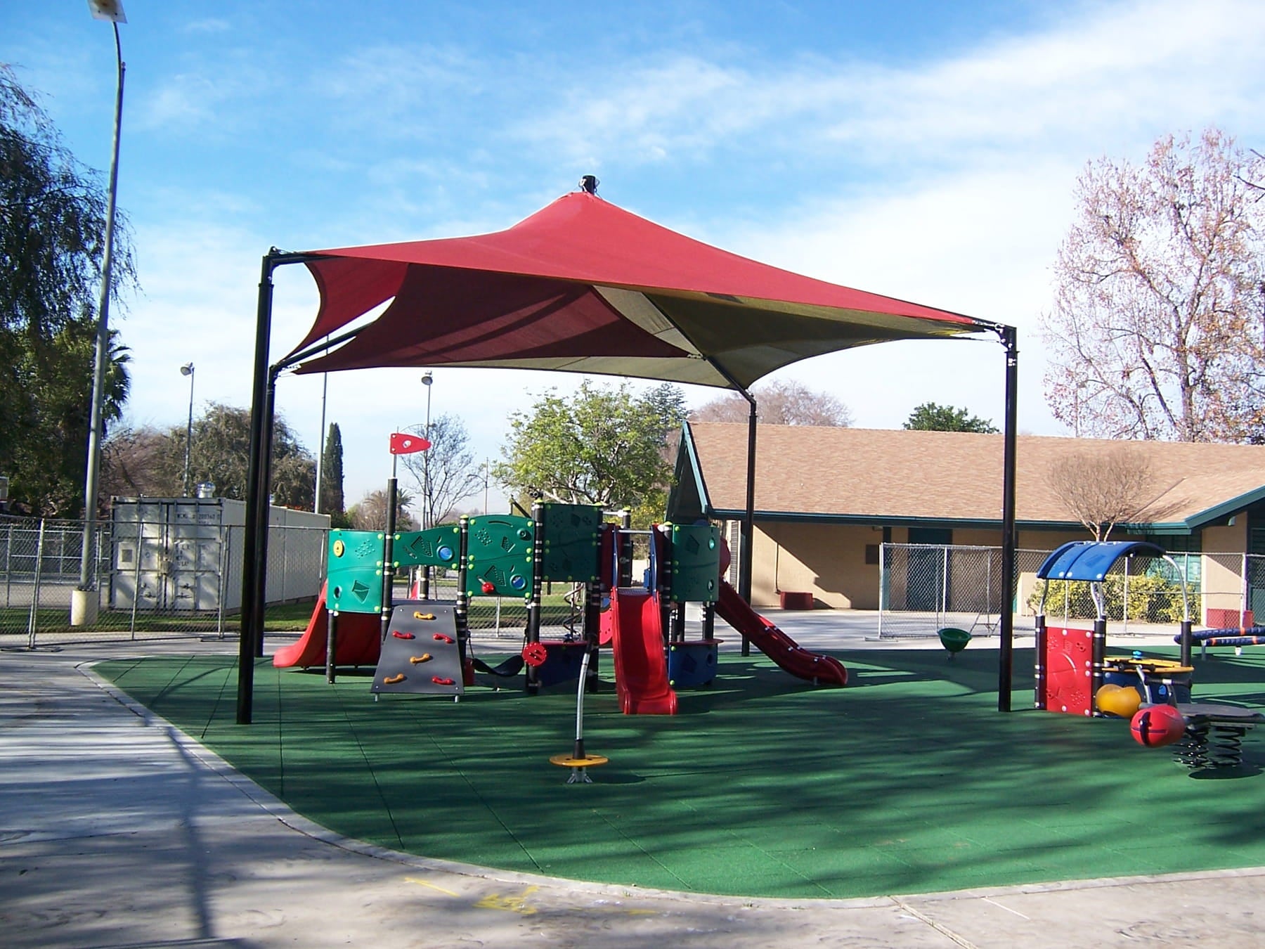 Children's playground with a USA Shade Mariner Pyramid Shade canopy, slides, and play equipment on a sunny day.