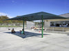 People sitting under a green USA Shade Two Post Hip Shade Structure in an outdoor area with a building in the background.