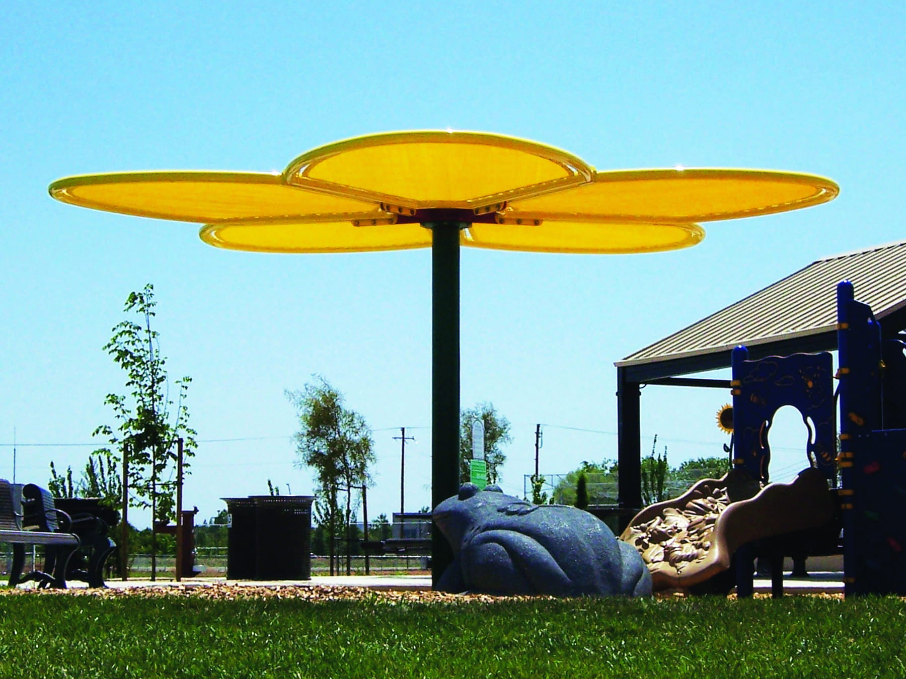 Children's playground with a large yellow USA Shade Flower Shade Structure and slide on a clear day.