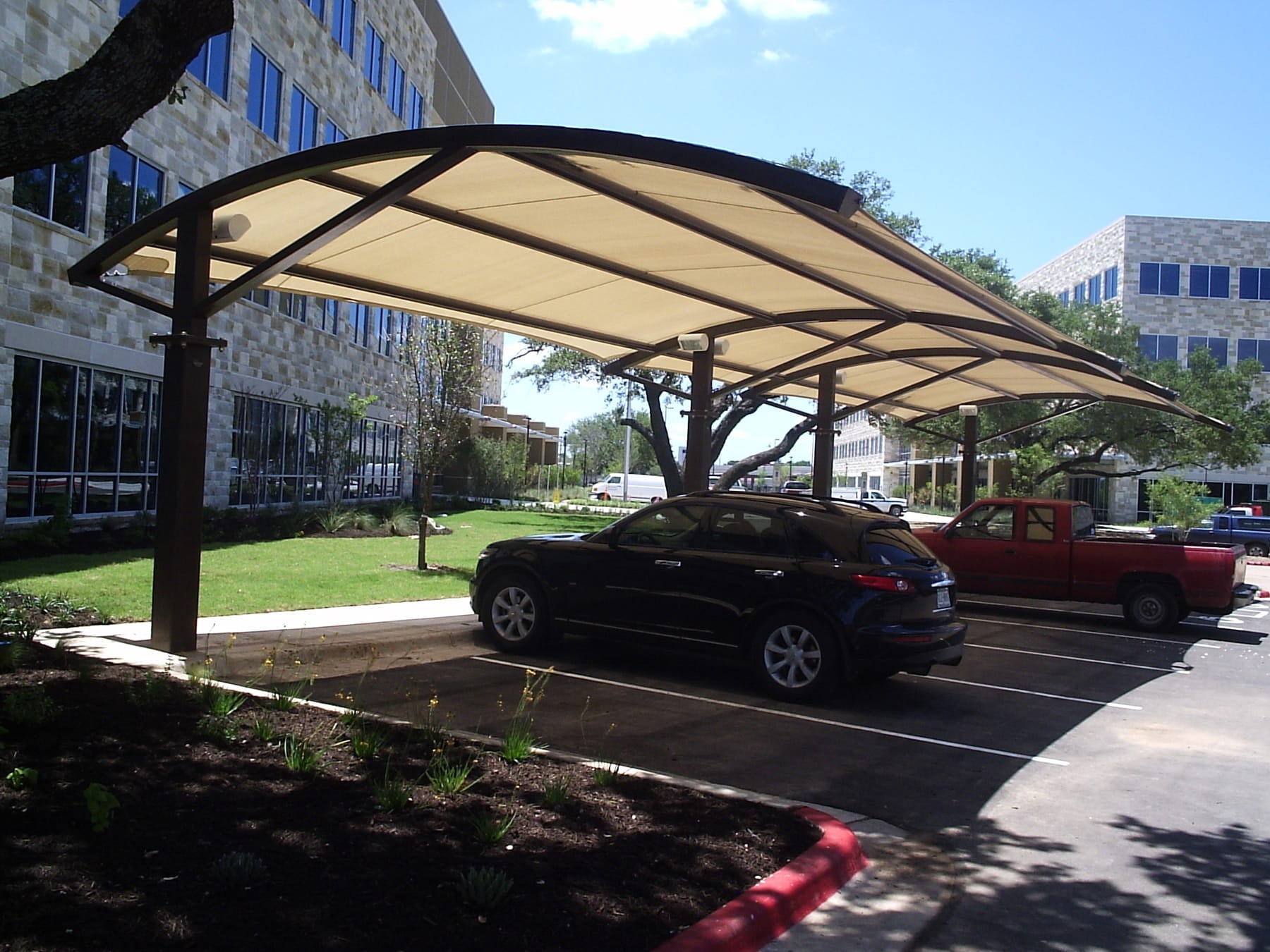 Car parked under a USA Shade Panorama Cantilever in a parking lot with a building in the background