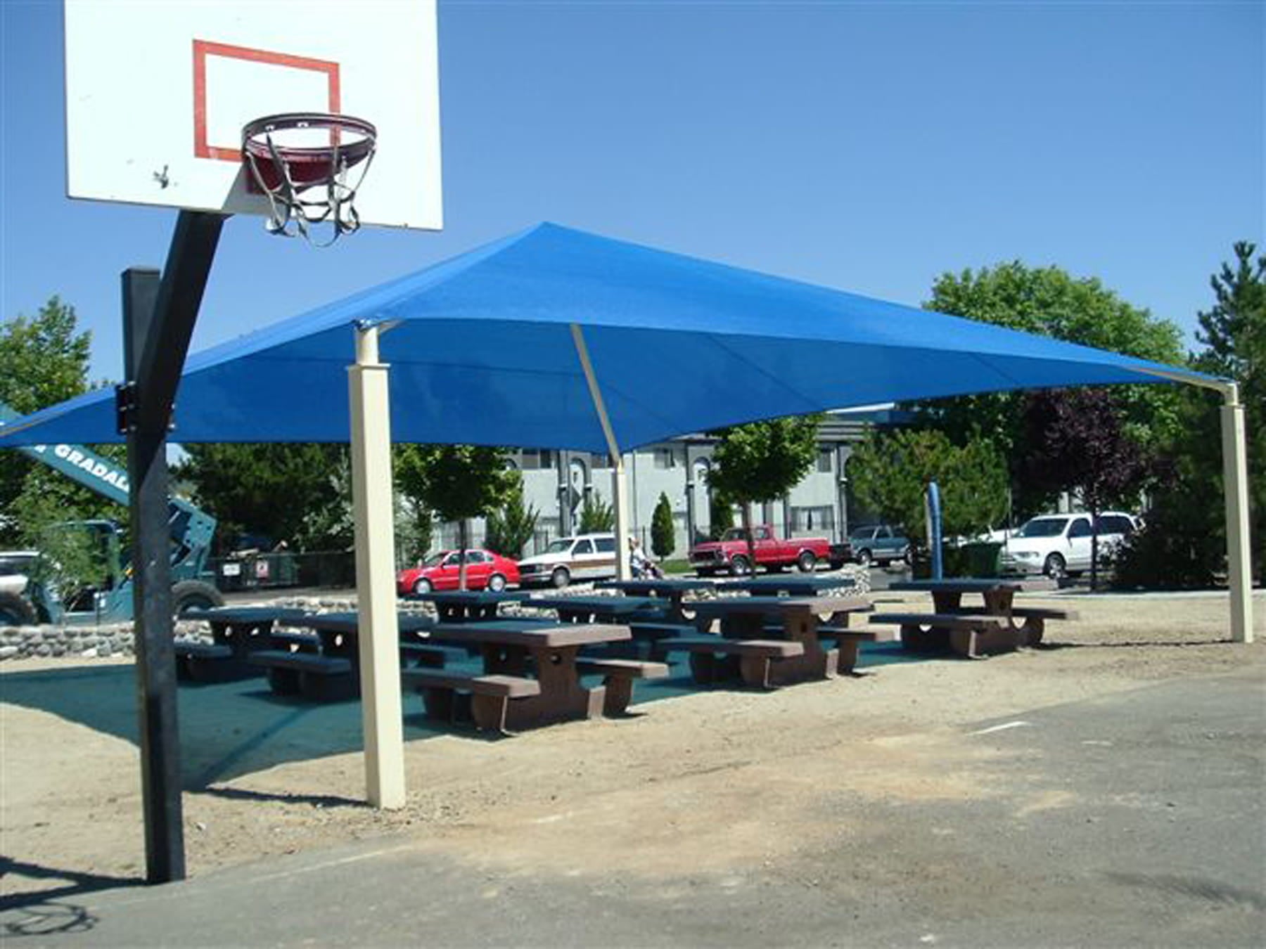 Blue USA Shade Pyramid Shade over picnic tables with a basketball hoop in the background