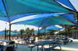 Outdoor seating area with blue USA Shade Mariner Pyramid Shade over picnic tables.