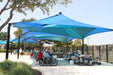 Outdoor shaded area with people sitting at picnic tables under large blue USA Shade Mariner Pyramid Shade.