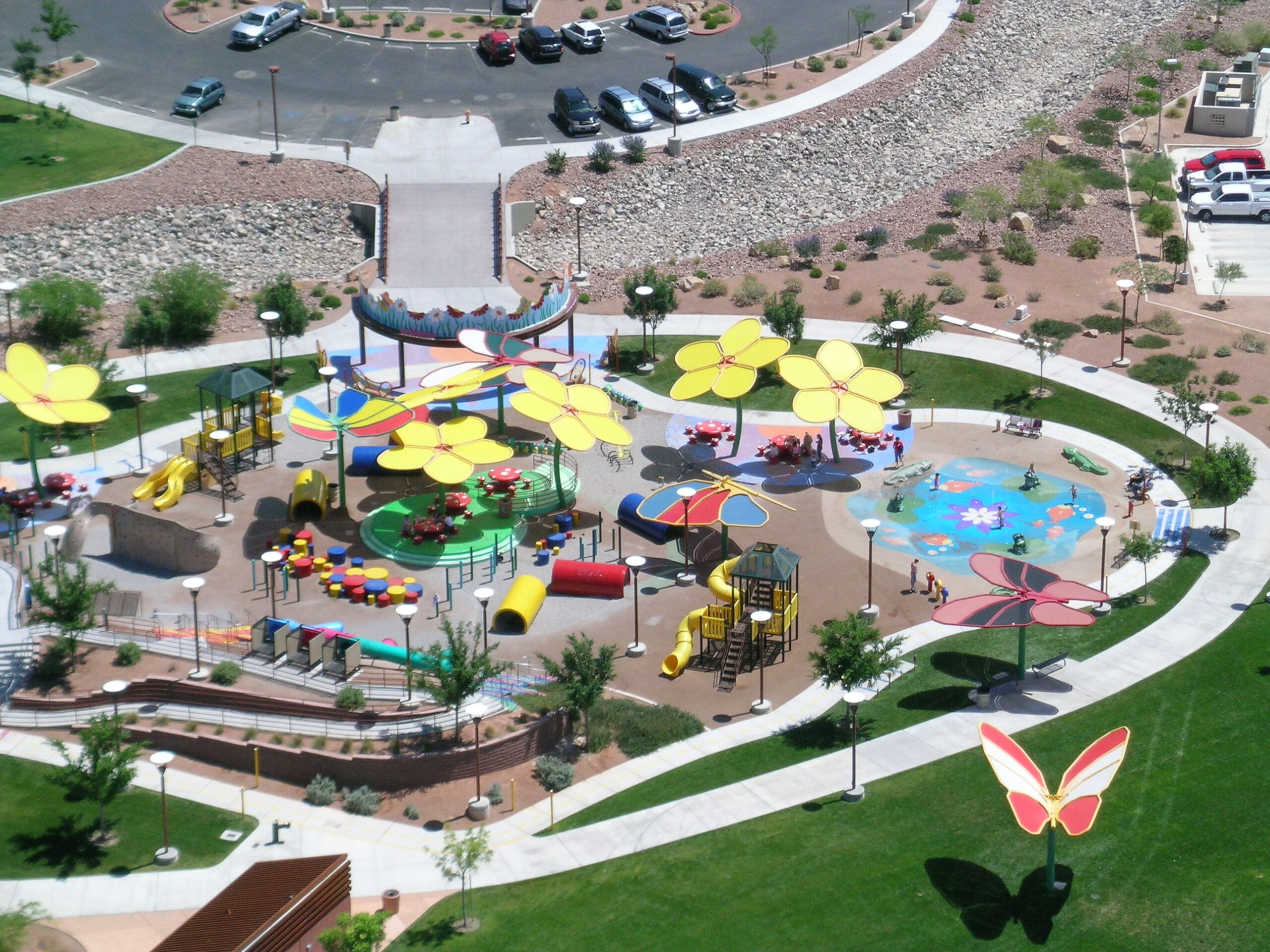 Colorful playground with various play structures and USA Shade Butterfly Wings Shades in a park setting.