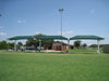 Three green USA Shade Full Hip Cantilever Shades on a grassy field with vehicles and a building in the background.