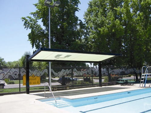 Pool area with a USA Shade Slanted Cantilever Framed covered seating area and trees in the background