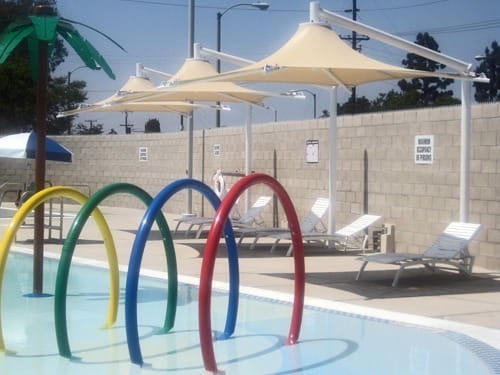 Colorful pool toys by a pool with lounge chairs and USA Shade Solana Cantilevers in the background.