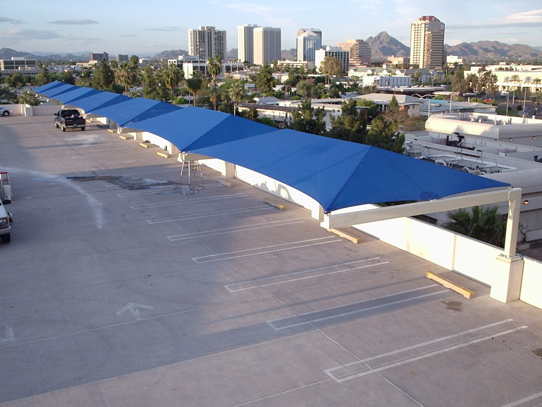 Blue USA Shade Full Hip Cantilever Shades over a parking lot with cityscape in the background