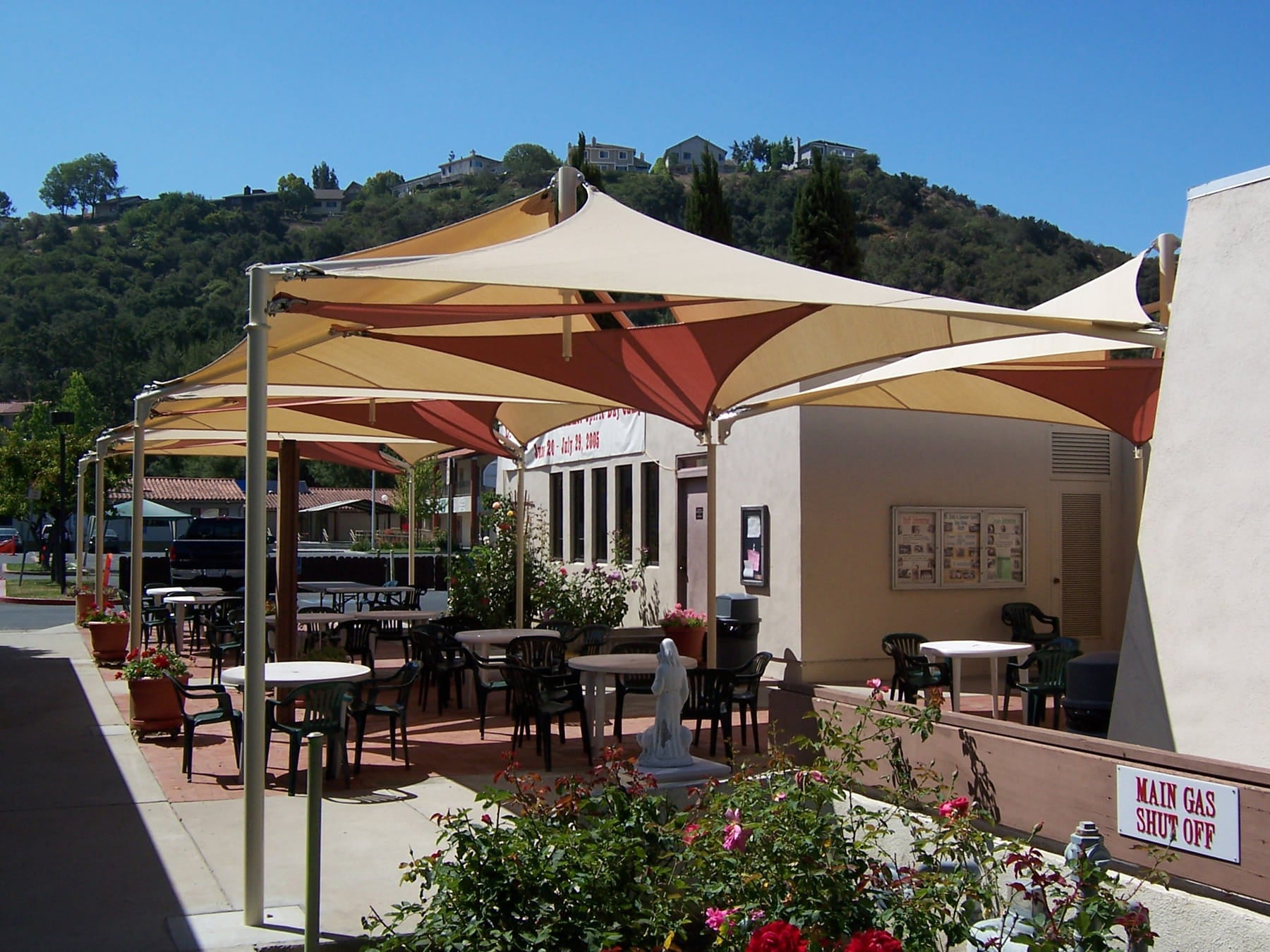 Outdoor seating area with tables, chairs, and large USA Shade Mariner Pyramid Shade under a clear blue sky.