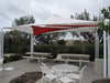 Outdoor patio area with a large red and white USA Shade Mariner Pyramid Shade, tables, and chairs.
