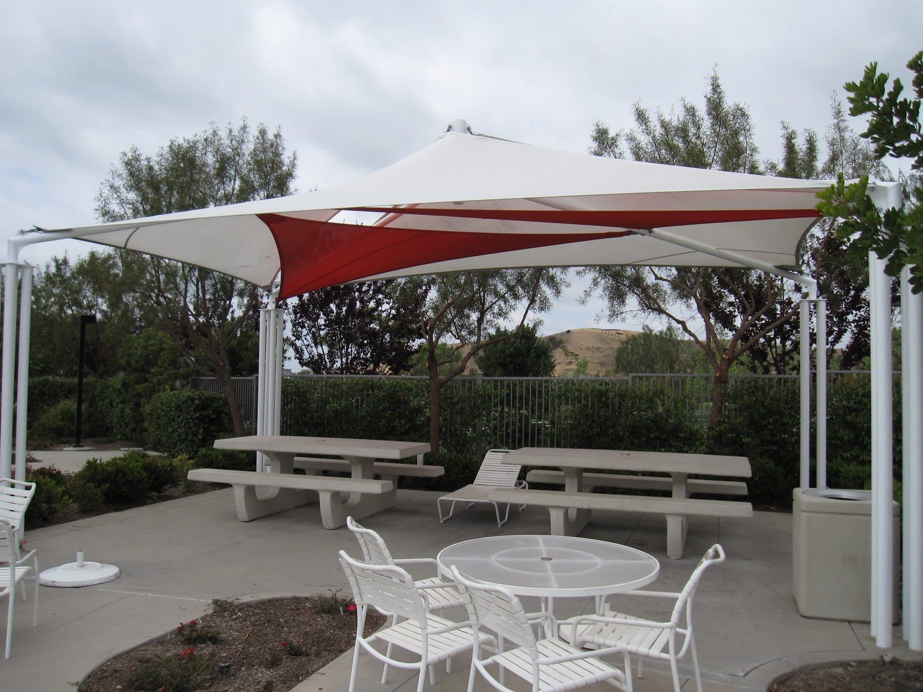 Outdoor patio area with a large red and white USA Shade Mariner Pyramid Shade, tables, and chairs.