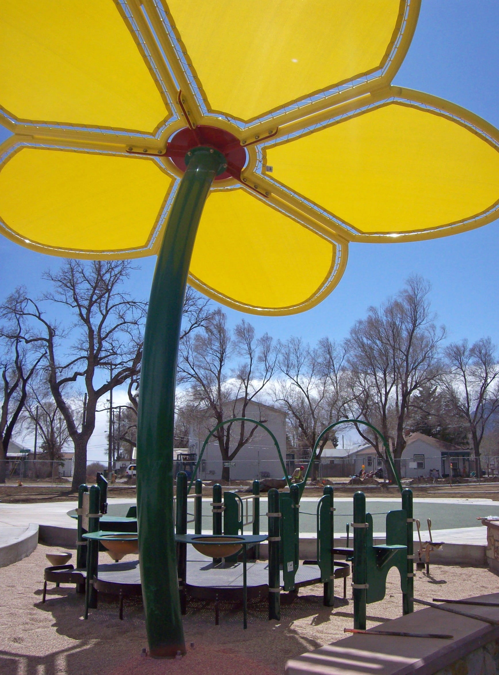 Children's playground structure with a yellow USA Shade Flower Shade Structure in an outdoor setting.