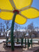 Children's playground structure with a yellow USA Shade Flower Shade Structure in an outdoor setting.