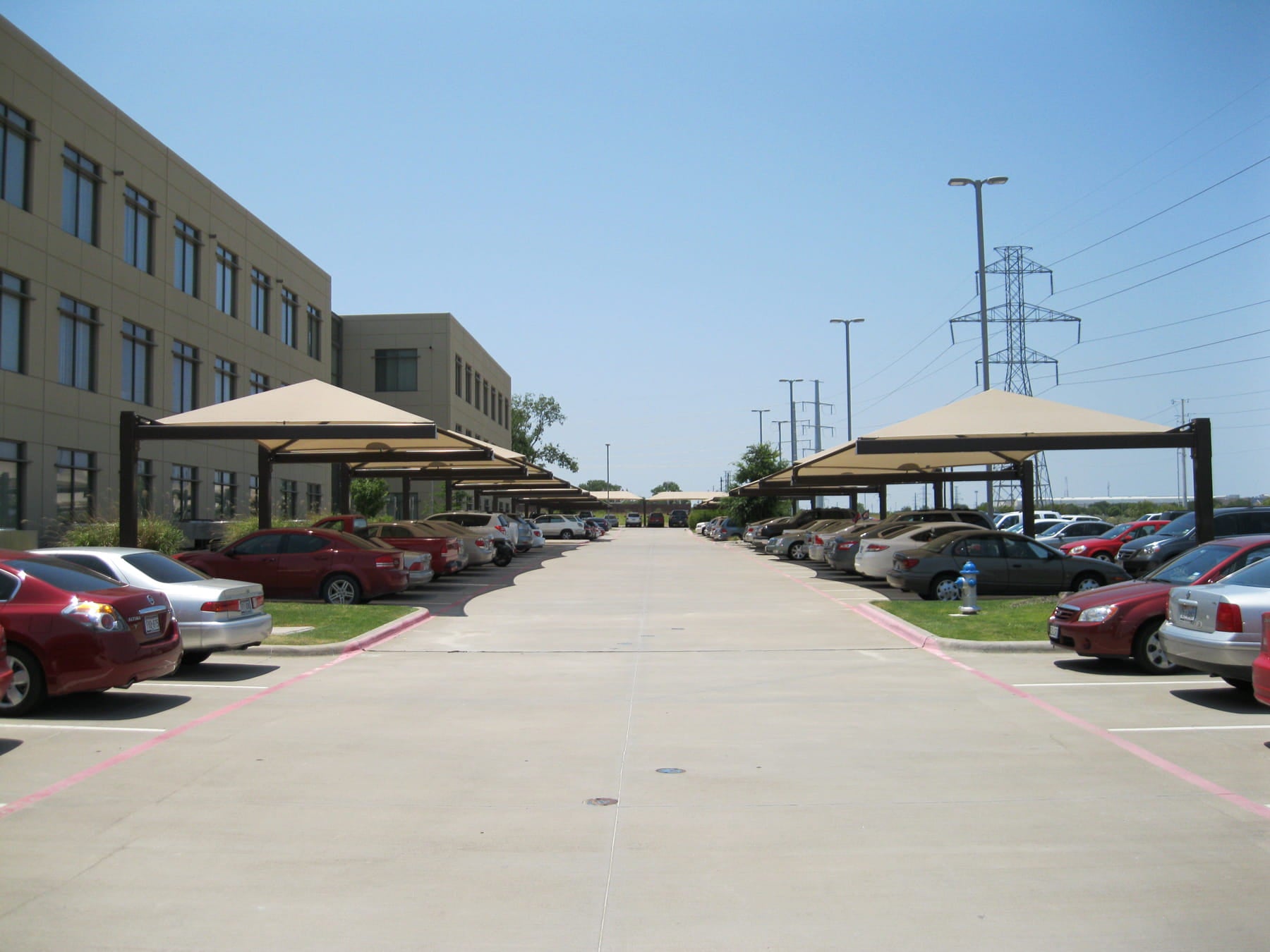 Parking lot with cars and USA Shade Full Hip Cantilever Shade covering car areas under a clear blue sky