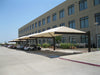 Carport with beige USA Shade Full Hip Cantilever Shades in front of a building with large windows on a clear day.