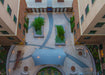A courtyard with a geometric design, plants, and a large blue USA Shade Aquarius Shade structure.