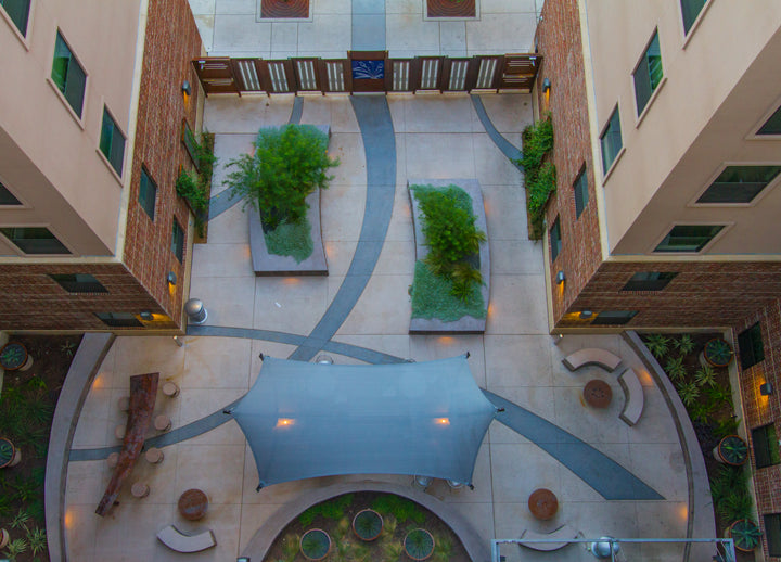A courtyard with a geometric design, plants, and a large blue USA Shade Aquarius Shade structure.