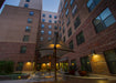 Evening view of a courtyard with outdoor furniture including USA Shade Aquarius Shade and lit buildings