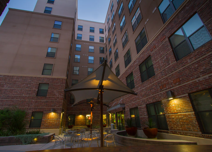 Evening view of a courtyard with outdoor furniture including USA Shade Aquarius Shade and lit buildings