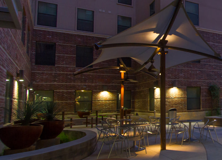 Outdoor patio area with tables, chairs, and USA Shade Aquarius Shade at night.
