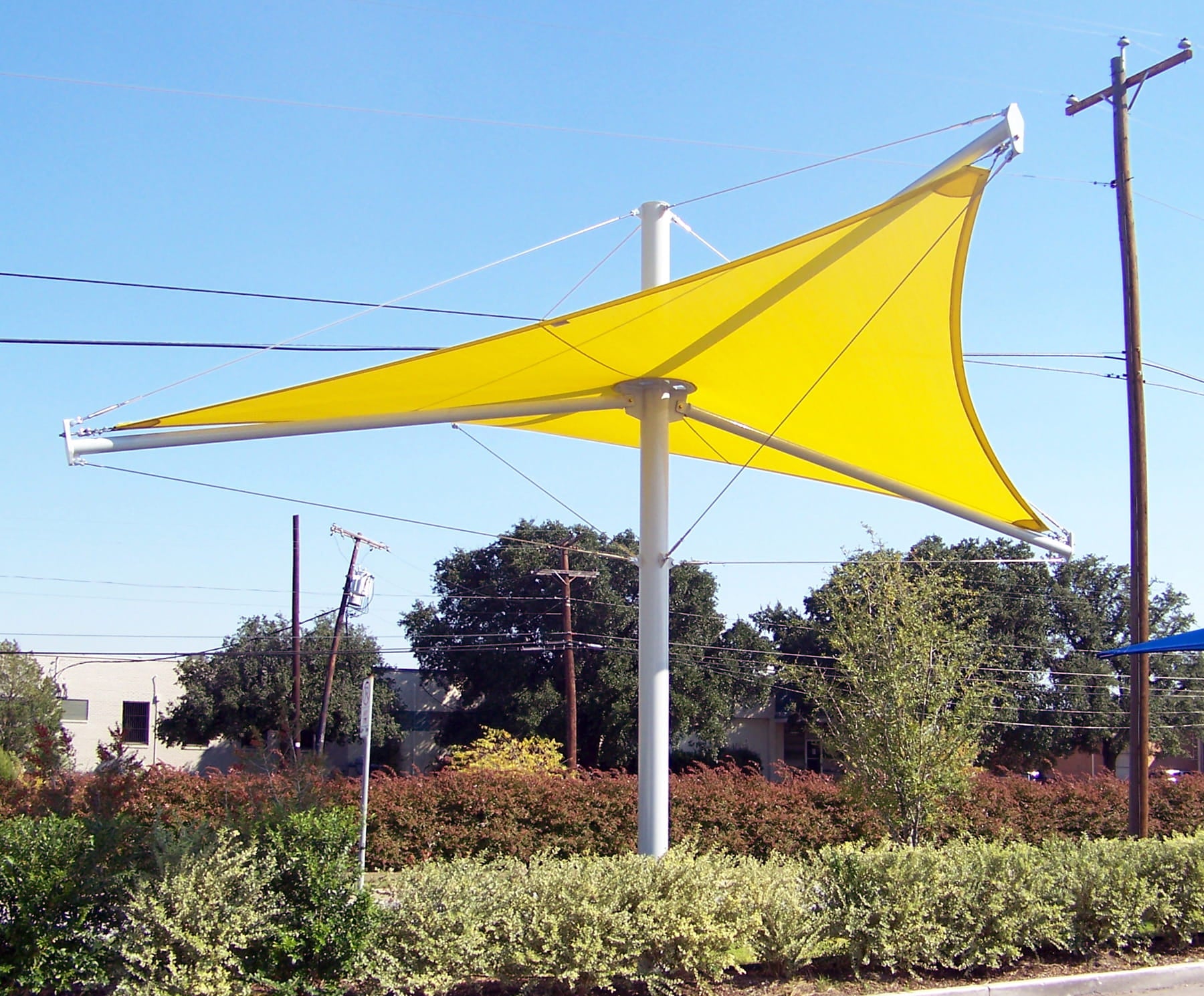 Yellow USA Shade Aurora Shade sail attached to a pole with power lines and trees in the background
