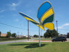 USA Shade Butterfly Wings Shade with blue and yellow wings on a grassy area under a clear blue sky.