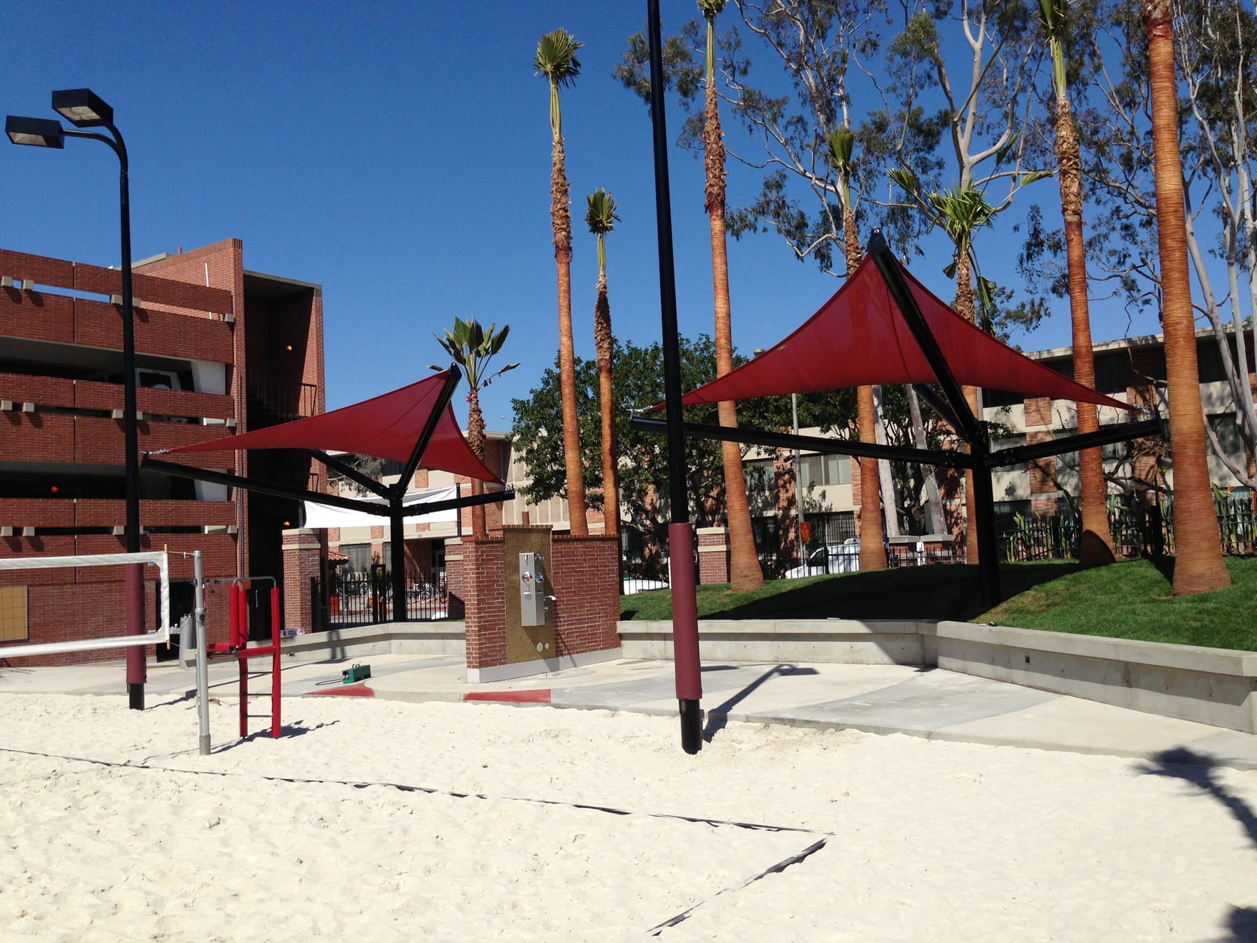 Outdoor playground area with red USA Shade Arbor Shade sails and palm trees under a clear blue sky.