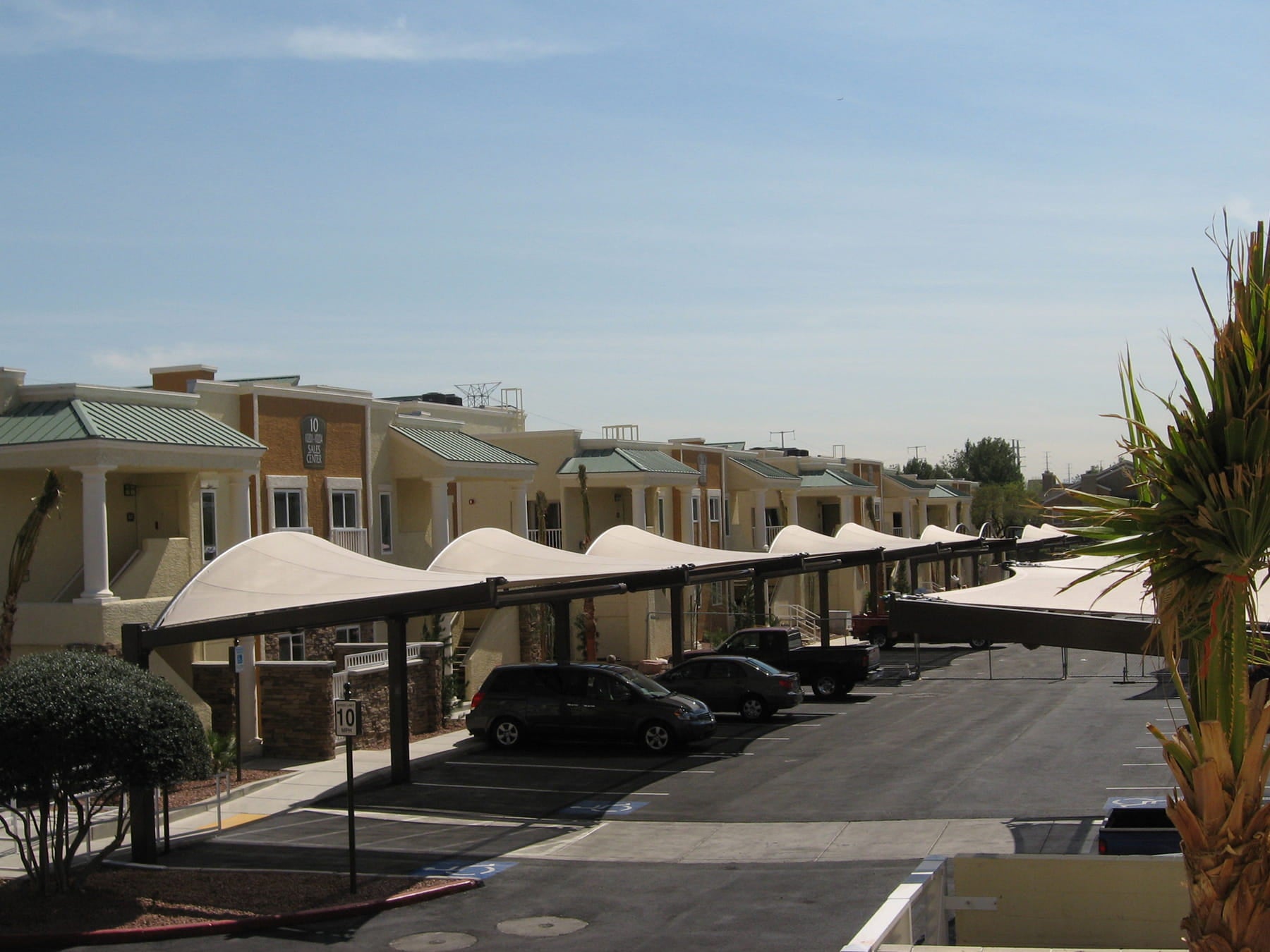 Parking lot with USA Shade Cypress Cantilevers, cars and a building in the background under a clear blue sky.