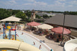 Outdoor pool area with slides, USA Shade Coolbrellas, and people near a clock tower.