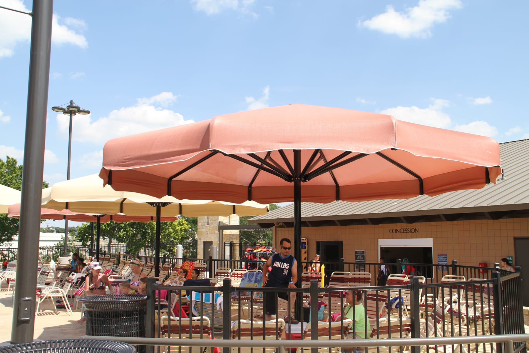 Large pink USA Shade Coolbrella in an outdoor setting with people and chairs under it.