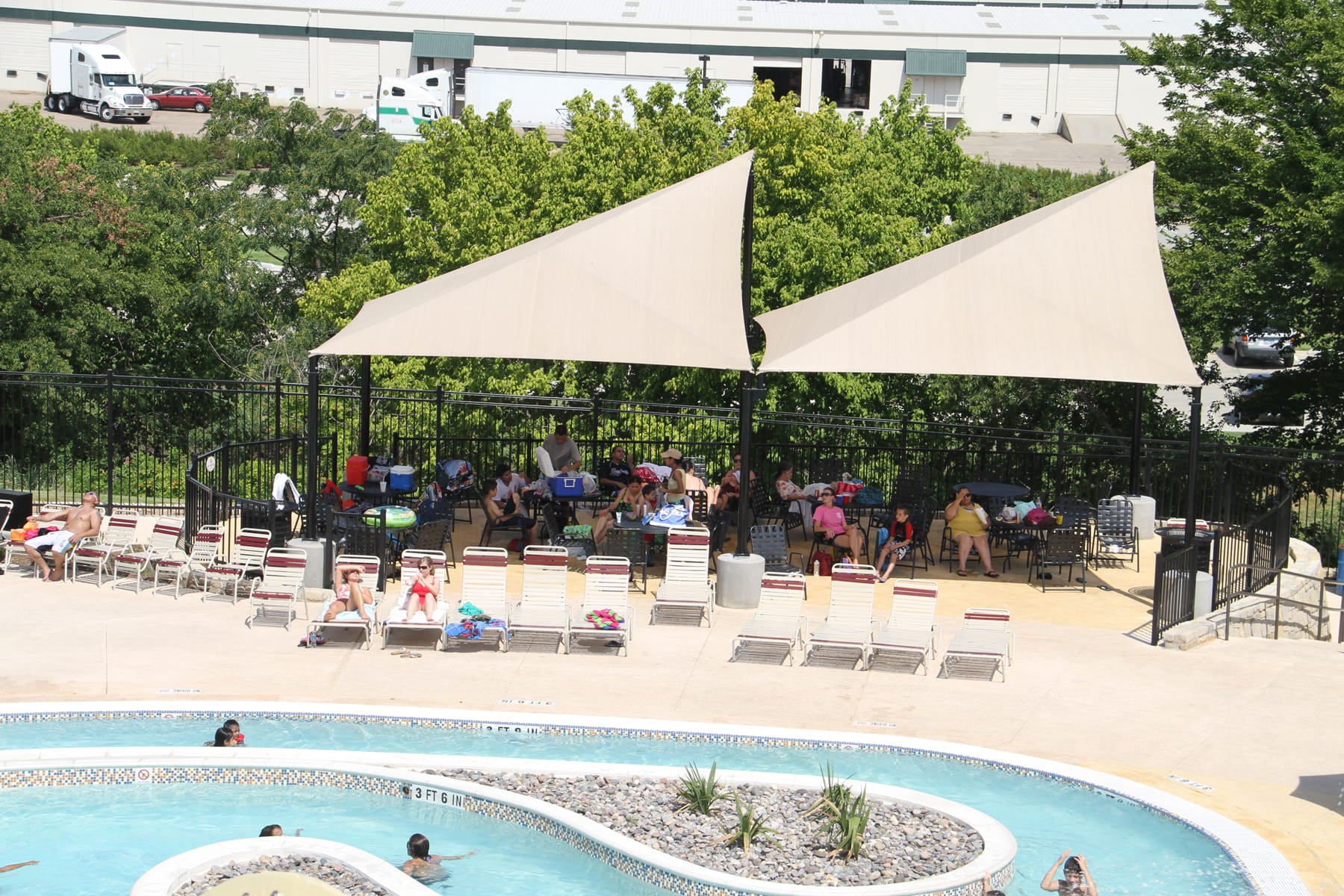 People gathered around a pool under USA Shade Wave Shades and siiting on chairs
