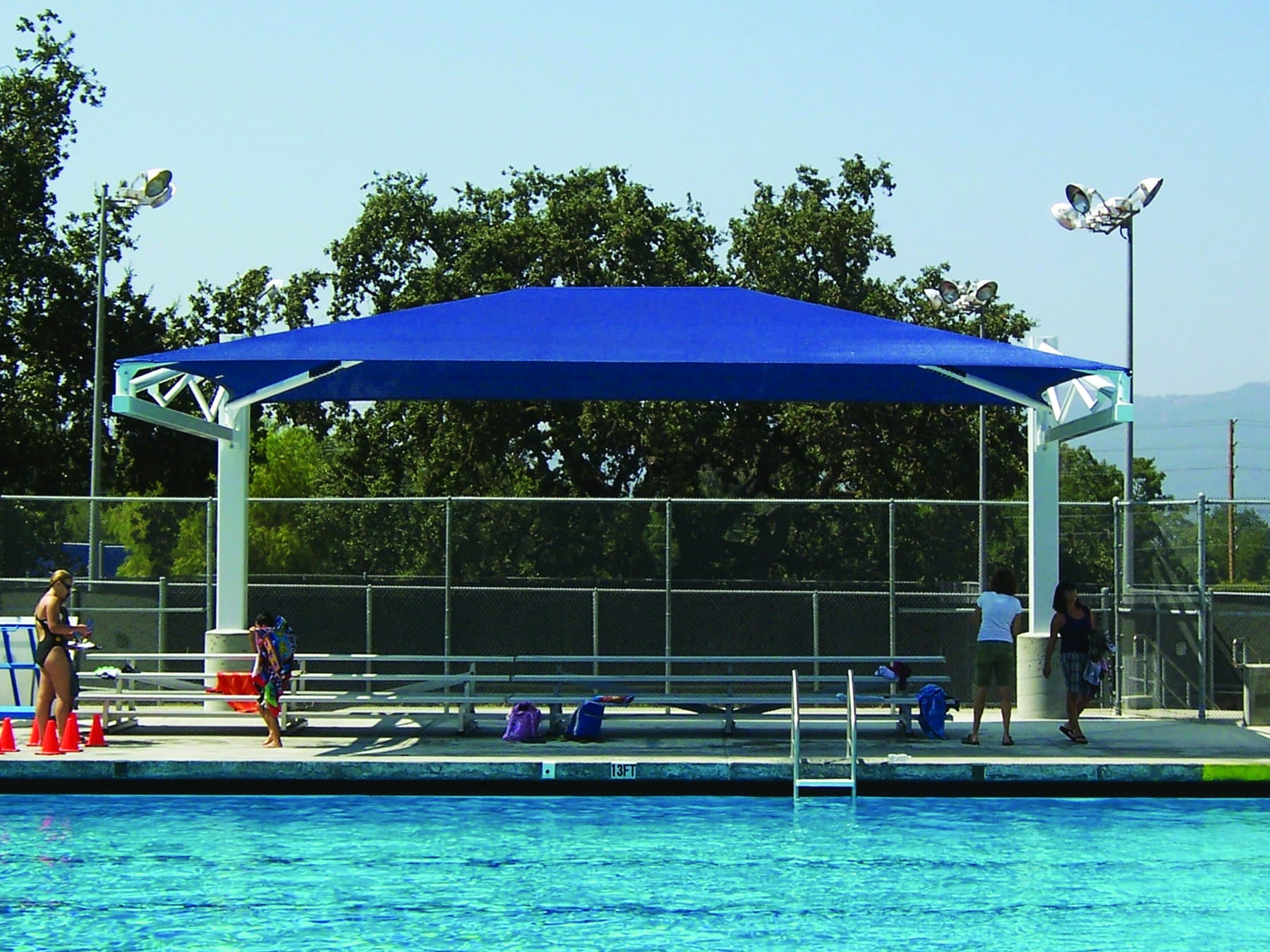 Blue USA Shade Tri-Truss Cantilever over a pool area with people around