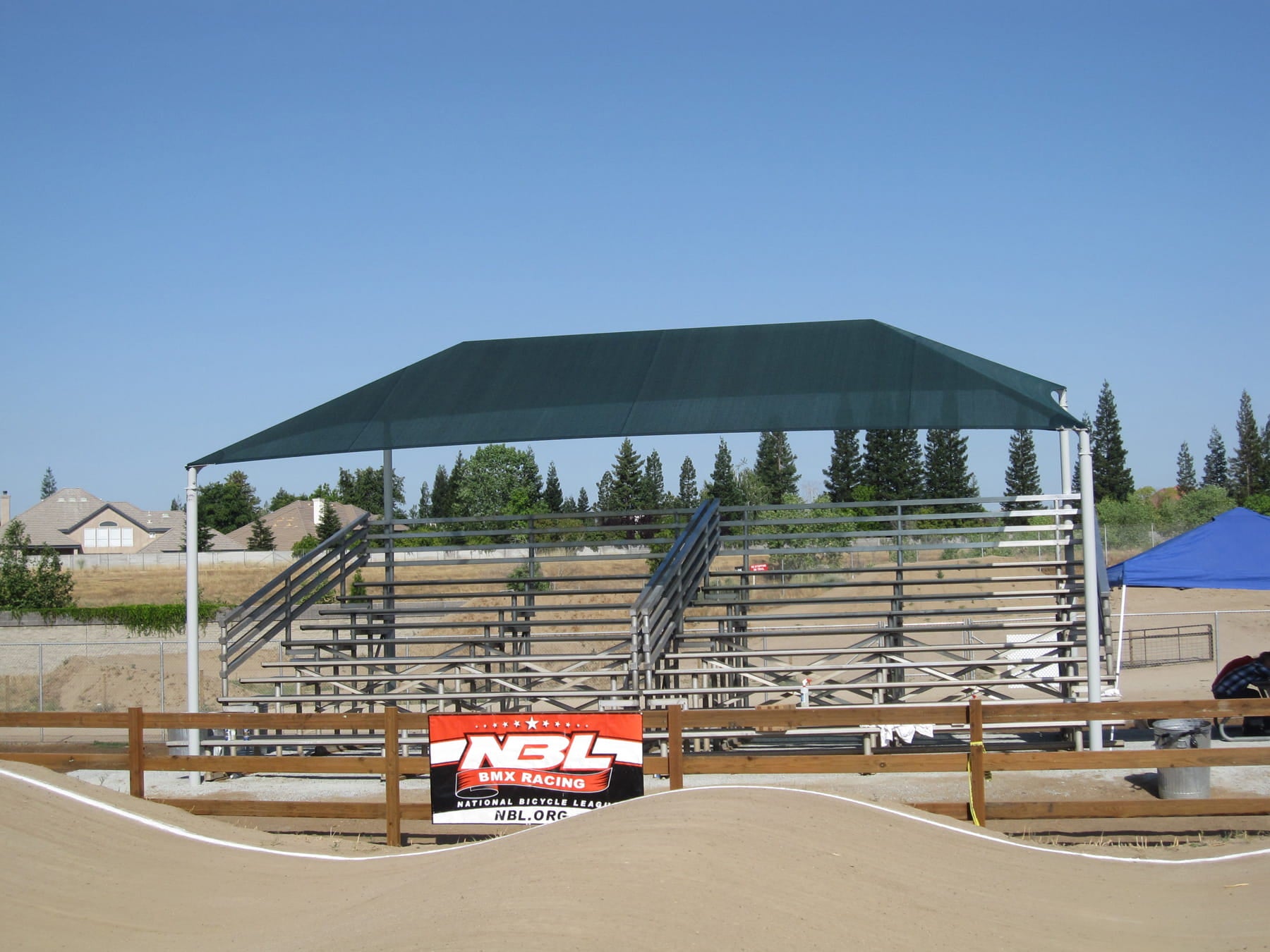 Outdoor sports facility with a green USA Shade Slant Hip and bleachers under a clear blue sky.